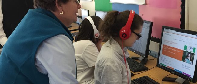 A teacher looking at a student who is using bookshare in audio format