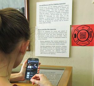 a person scanning a qr code displayed on the wall with their phone to watch the exhibit's ASL video tour