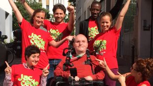 a group of people smiling. There is a person in the middle in a wheelchair.