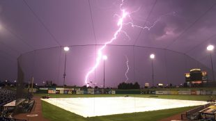 photo of a softball field with lightning in the background