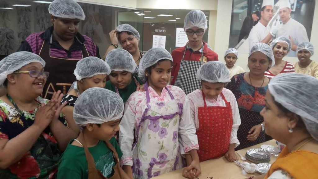 a group of children inside a kitchen listening to baking instructions from an adult mentor.