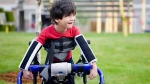 a young boy seen holding a crutches like support accessory and smiling