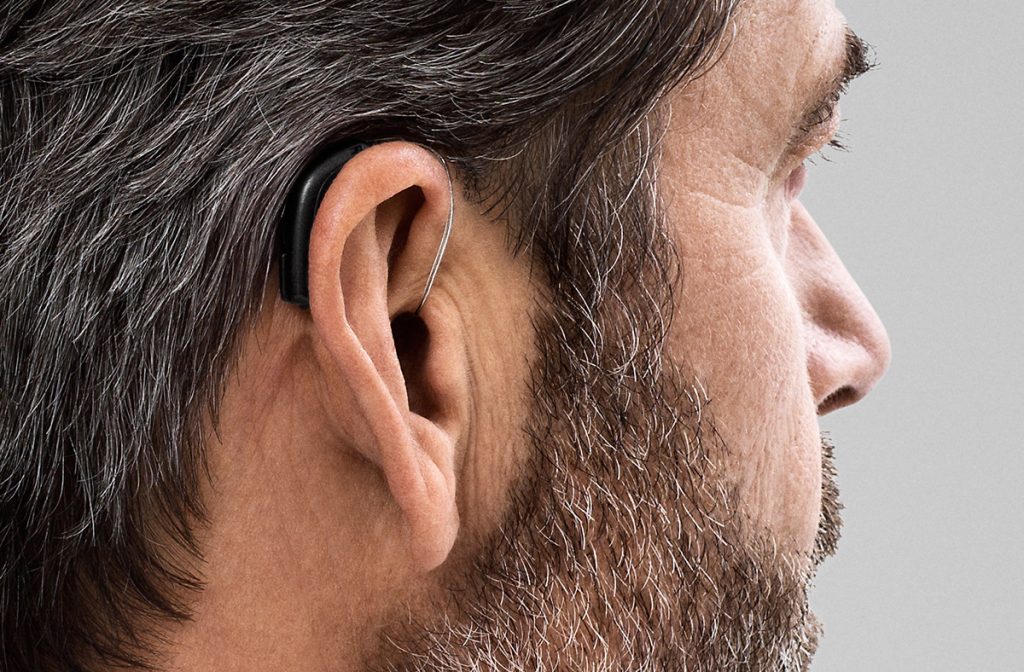 photo showing a person wearing Oticon Opn. The photo depicts how small the hearing aids are, and can be discretely hidden behind the ear.