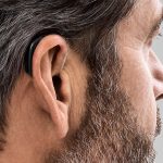 photo showing a person wearing Oticon Opn. The photo depicts how small the hearing aids are, and can be discretely hidden behind the ear.