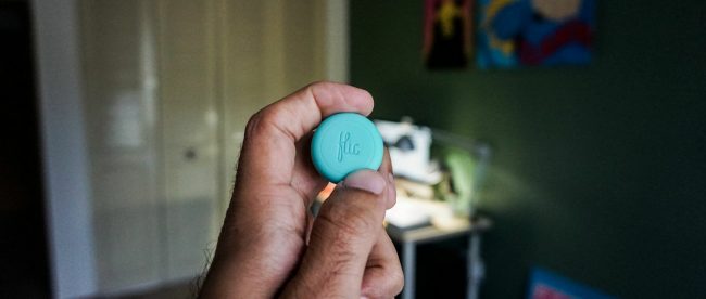 Close up of a person holding Flic - a small, round, smart wireless button.