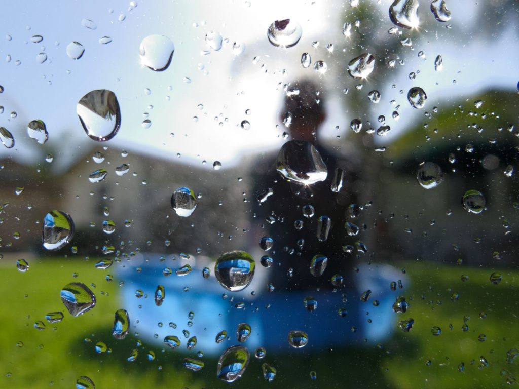 water droplets on a window. In the background (outside, in the yard), is Bruce's son in a small water pool.