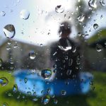 water droplets on a window. In the background (outside, in the yard), is Bruce's son in a small water pool.