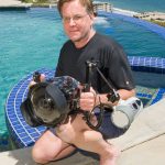 Photo of Bruce Hall by a swimming pool. He is holding a camera in his hand.