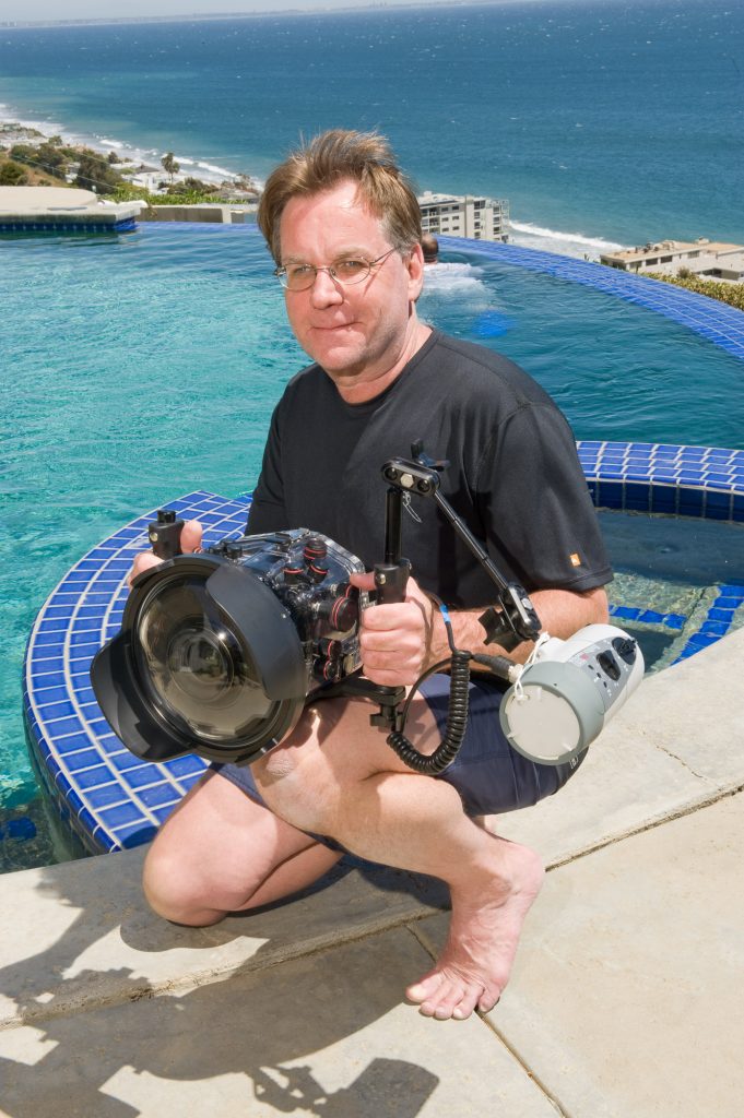 Photo of Bruce Hall by a swimming pool. He is holding a camera in his hand.