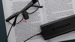 a pair of glasses with orcam myeye attached to the right stem resting on a book