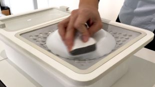 a person seen cleaning a dish with one hand. This dish is placed on the surface of the OneWare attachment used for cleaning dishes.