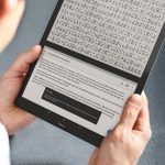 A person is holding a blitab in his hands. There is text displayed in the bottom screen, and the braille equivalent of it is displayed on the top screen.