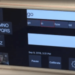 interface visible to the interpreter. It shows the word "go" in the top field. Right below it are four words that have been predicted by the app - "go", "in", "how", and "lot". Below these words are the field that shows the entire chain of words in this communication. To the left is the layout of the e-tran board. Right below it is the person's face captured by the phone camera. At the bottom right are options "pause", "calibrate" and settings.