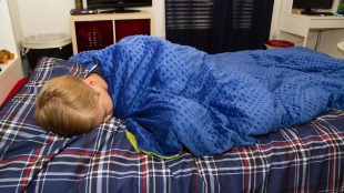 a child in bed with the weighted blanket wrapped around him.