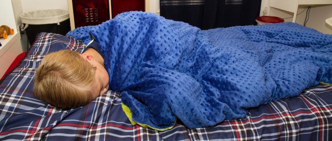 a child in bed with the weighted blanket wrapped around him.