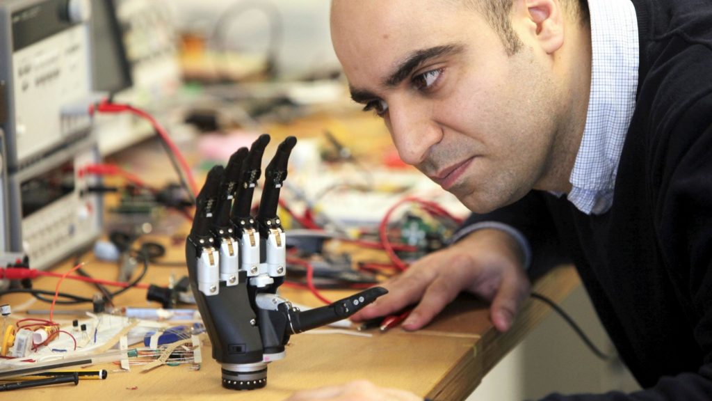 a man looking closely at the intuitive hand. It is seen resting on a desk with lots of cables in the background.