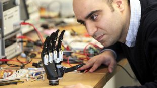 a man looking closely at the intuitive hand. It is seen resting on a desk with lots of cables in the background.