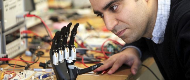 a man looking closely at the intuitive hand. It is seen resting on a desk with lots of cables in the background.