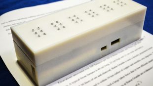 photo of current version of tactile placed on top of a book and displaying six characters in braille.