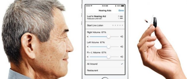 Photo shows the side profile of a man to the left, an IPhone in the middle, and a hand holding a cochlear implant). The screen on the iPhone shows volume settings for hearing aids.