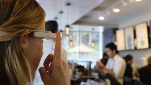 a woman in a coffees shop is seen pressing the button on her aira smartglasses.