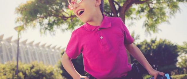 A child wearing a megenta shirt and glasses seen holding a walker. He is smiling.