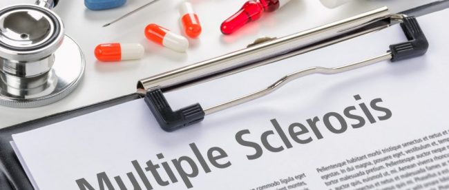 a clipboard with a sheet titled multiple sclerosis. A bunch of pills and a syringe are seen right next to it.