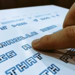 Close up of text in Braille Neue. A finger is seen on the text presumably of a blind person feeling the Braille bumps.