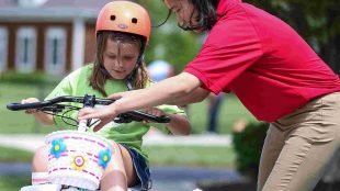 9 year old bella cates is seen on her bike. One of the students who designed the bike is seen adjusting her bike's handle bars.