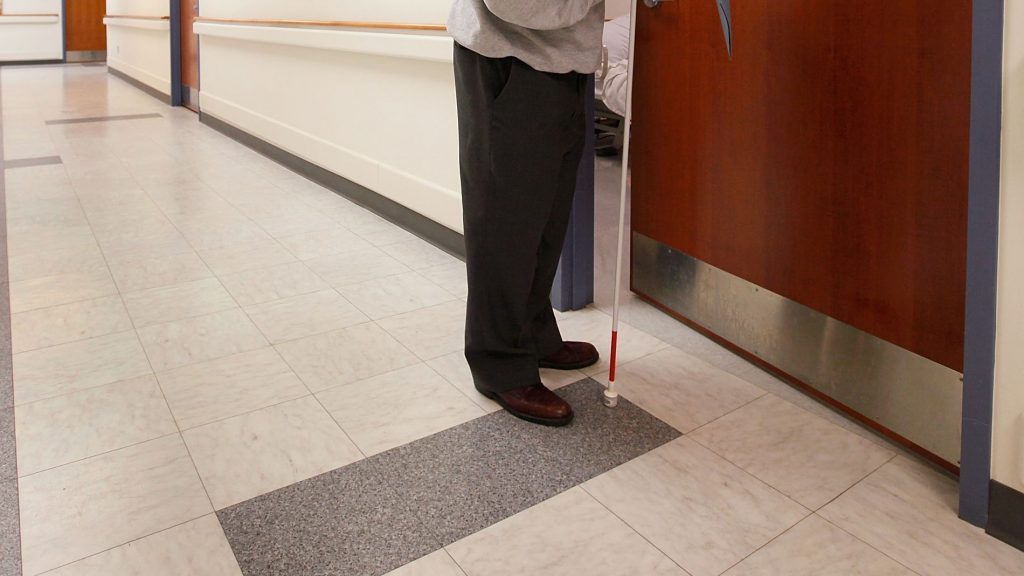 a blind person holding a white cane seen opening a door.