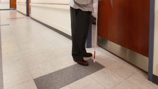 a blind person holding a white cane seen opening a door.