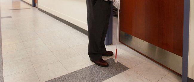 a blind person holding a white cane seen opening a door.