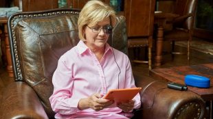 a woman seen sitting in a big leather chair, reading wearing seeBOOST and reading something on her tablet.