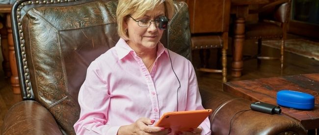 a woman seen sitting in a big leather chair, reading wearing seeBOOST and reading something on her tablet.