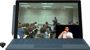 a computer screen showing a class in session. A professor is seen teaching a class full of students. On the bottom right corner of this video is an overlay with an interpreter seen signing the professor in real time.