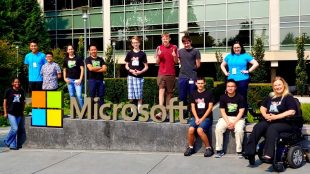 students posing for a photo. They are all seen standing around a physical microsoft logo at the microsoft campus.