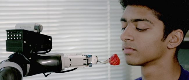 ADA points the fork with a strawberry in its prongs right in front of a user's mouth.