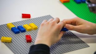 close up of a child's hands shown playing with braille lego blocks. Braille legos will have letters, numbers and punctuation printed on them as well so both sighted and blind children can play together.