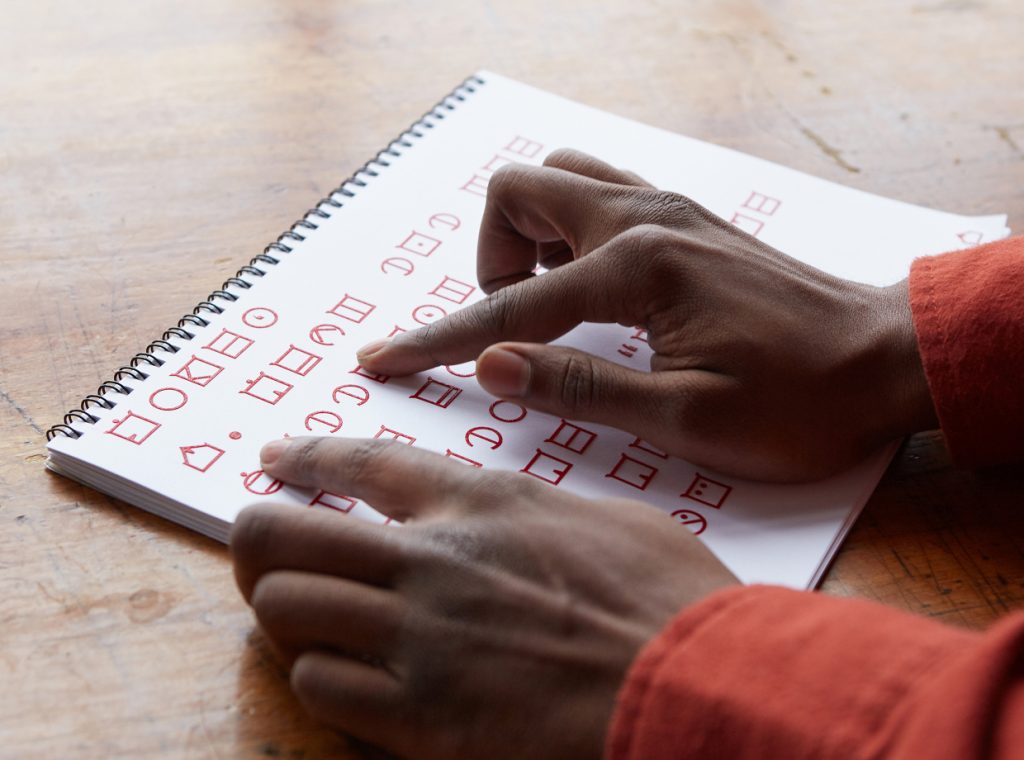 photo shows a person's right hand tracing letters on a paper printed in ELIA