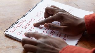 photo shows a person's right hand tracing letters on a paper printed in ELIA