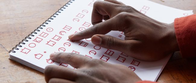 photo shows a person's right hand tracing letters on a paper printed in ELIA