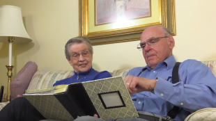 a woman who has alzheimer's sitting with her husband going through a photo album.