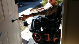 a man in a motorized wheelchair seen pulling on the t-pull door closer attached to a door.