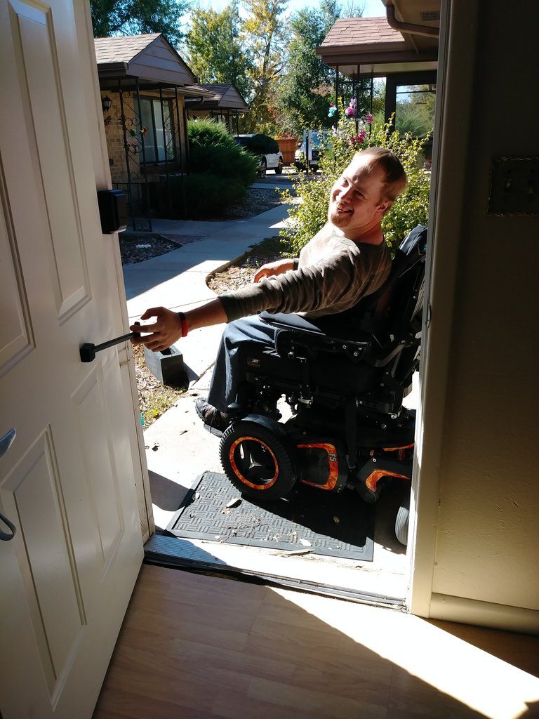 a man in a motorized wheelchair seen pulling on the t-pull door closer attached to a door.