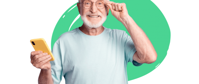 an elderly man seen smiling and holding a cell phone with yellow cover in his right hand adjusting his glasses with his left.