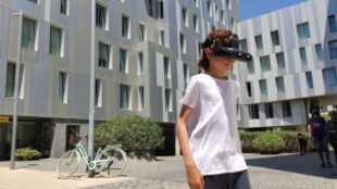 A young boy wearing a white t shirt seen wearing smart glasses outside a building