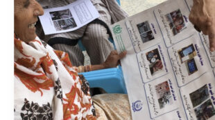 An elderly woman possibly from Pakistan seen looking at a poster and smiling.