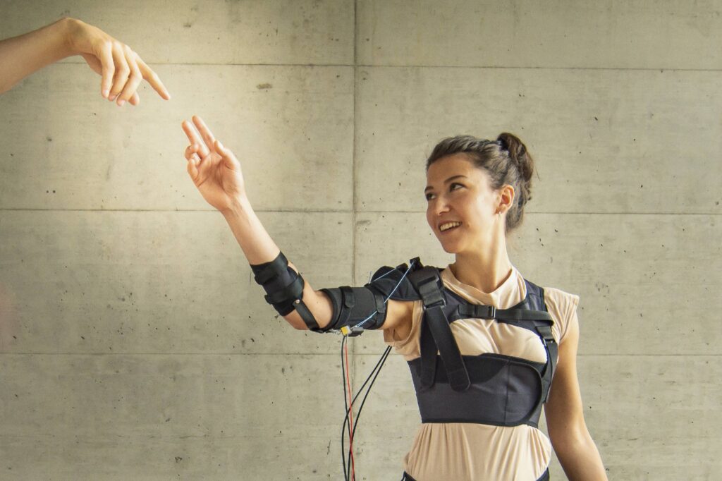 a woman seen wearing the myoshirt and raising her right hand. another hand of a person not in photo is reaching her hand.