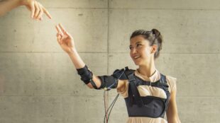 a woman seen wearing the myoshirt and raising her right hand. another hand of a person not in photo is reaching her hand.