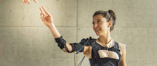 a woman seen wearing the myoshirt and raising her right hand. another hand of a person not in photo is reaching her hand.